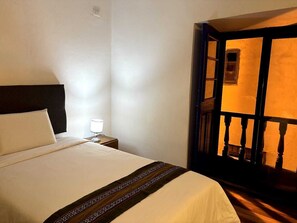 A hotel room with a bed, a nightstand, a lamp, and a view of a balcony with wooden railings. - Hostal Flor de Loto  (Cusco)