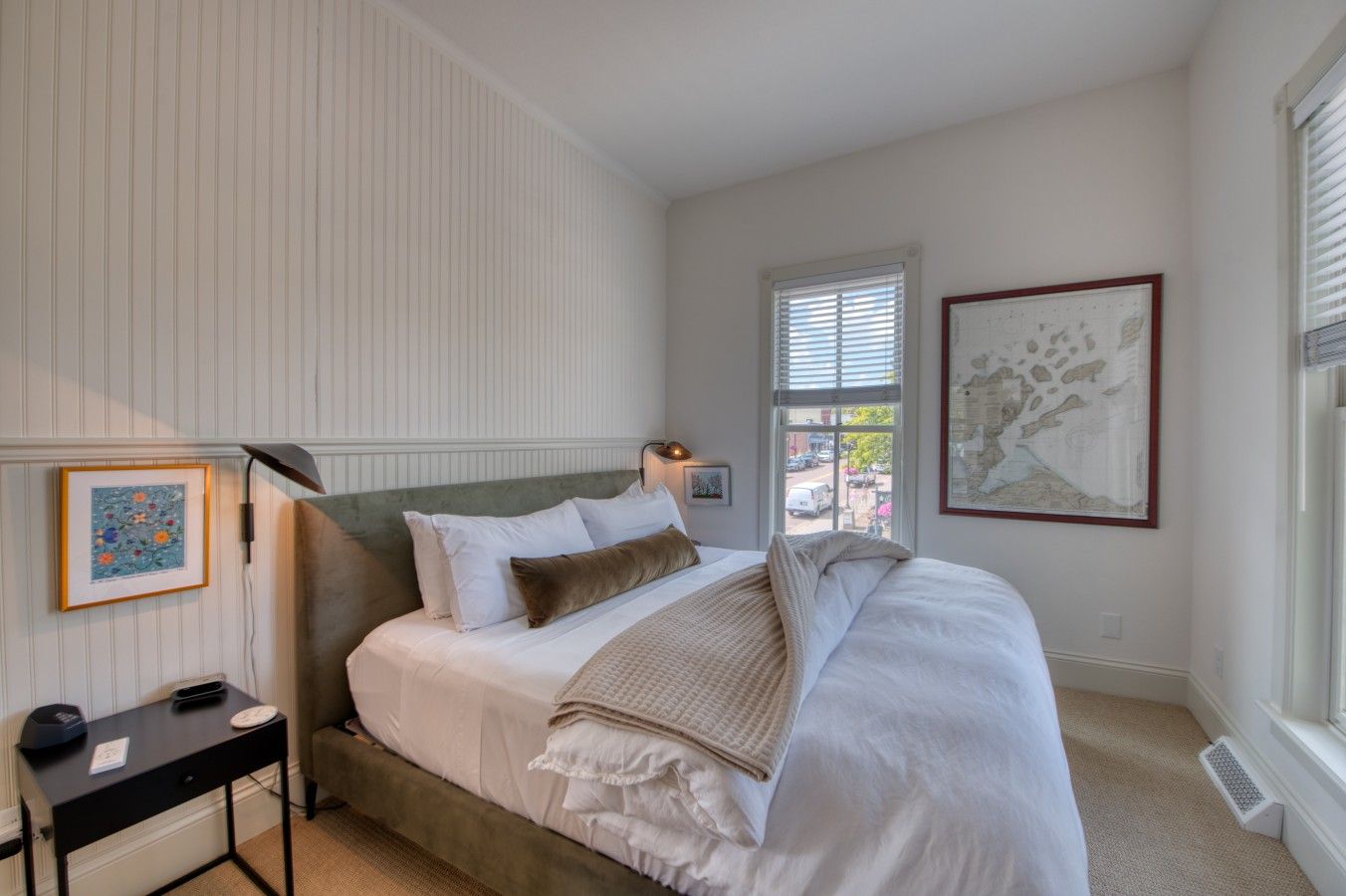 A bedroom with a bed, bedside table, lamp, and artwork.