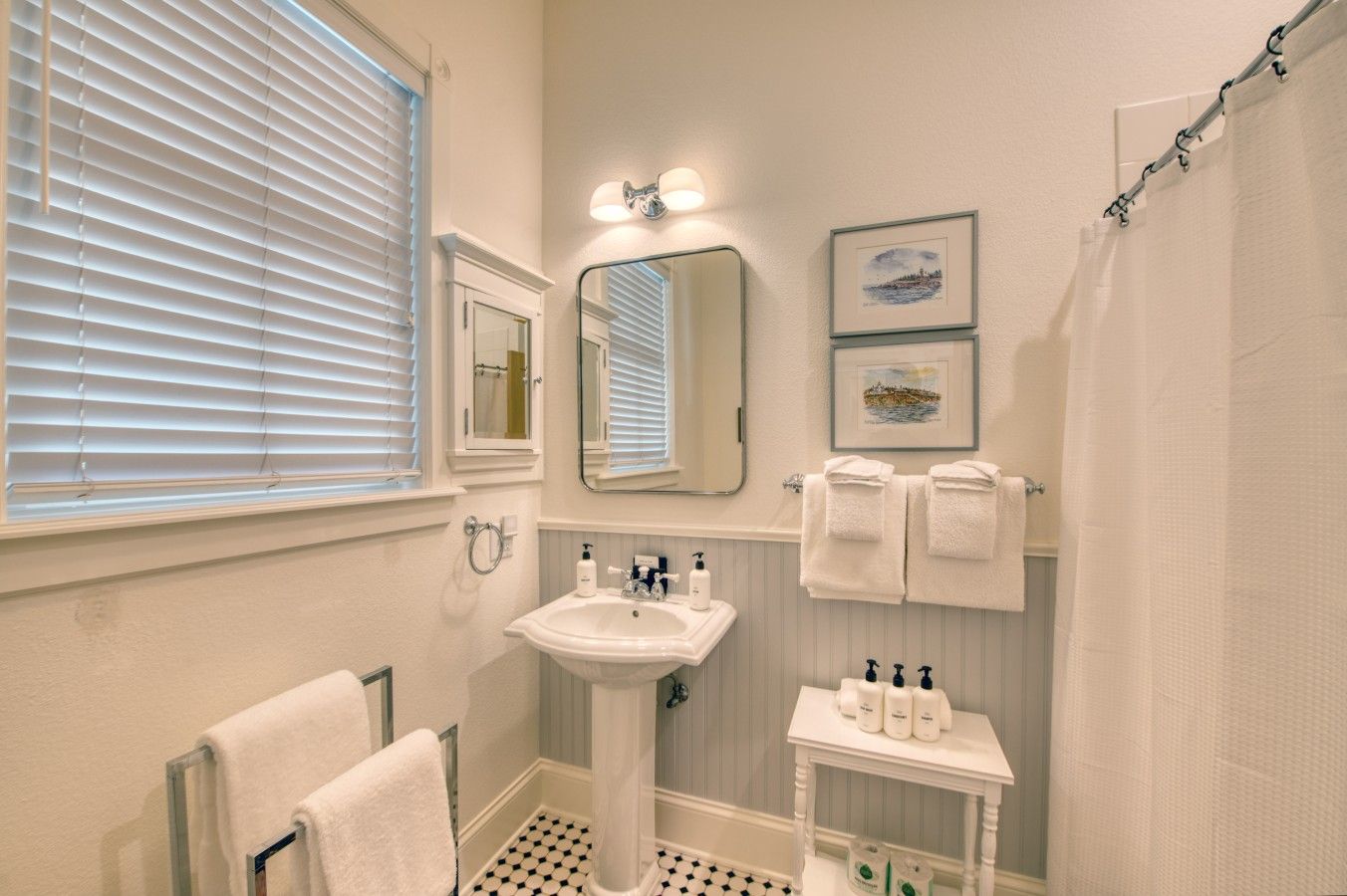 A bathroom with a pedestal sink, a mirror, a towel rack with towels, a small table with toiletries, and a shower curtain.