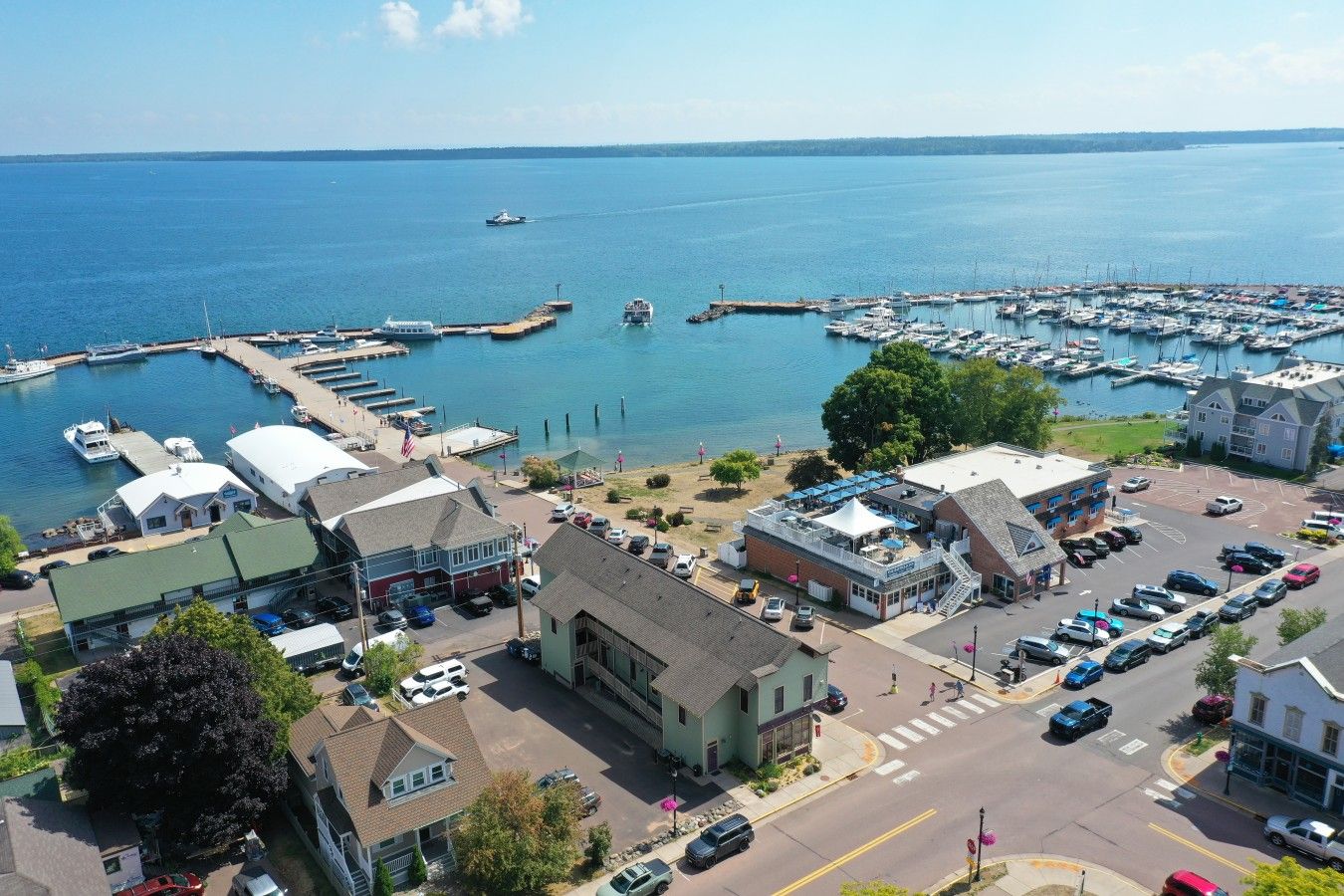 A marina with boats docked, a parking area, and buildings with commercial establishments.