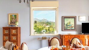 Un comedor con vistas a un paisaje montañoso a través de un ventanal grande, mobiliario de madera y un televisor a la derecha.