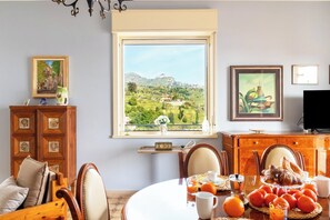 Ein Essbereich mit Blick auf eine gebirgige Landschaft durch ein großes Fenster, Holzmöbel und ein Fernseher auf der rechten Seite.