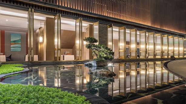Eine moderne Hotelhalle mit einem spiegelnden Pool, Zimmerpflanzen und einer Sitzecke.
