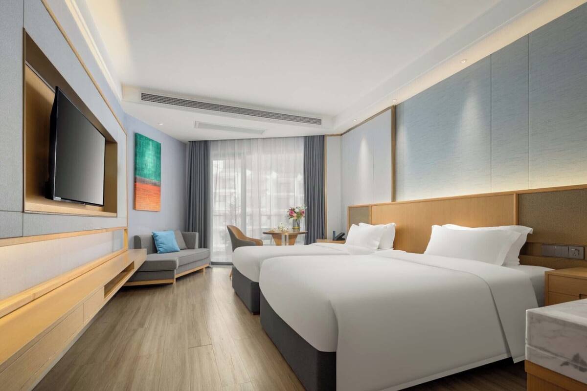 Ein modernes Hotelzimmer mit einem großen Bett, einem flachbildfernseher an der Wand, einer Couch und einem kleinen Tisch mit Blumen.