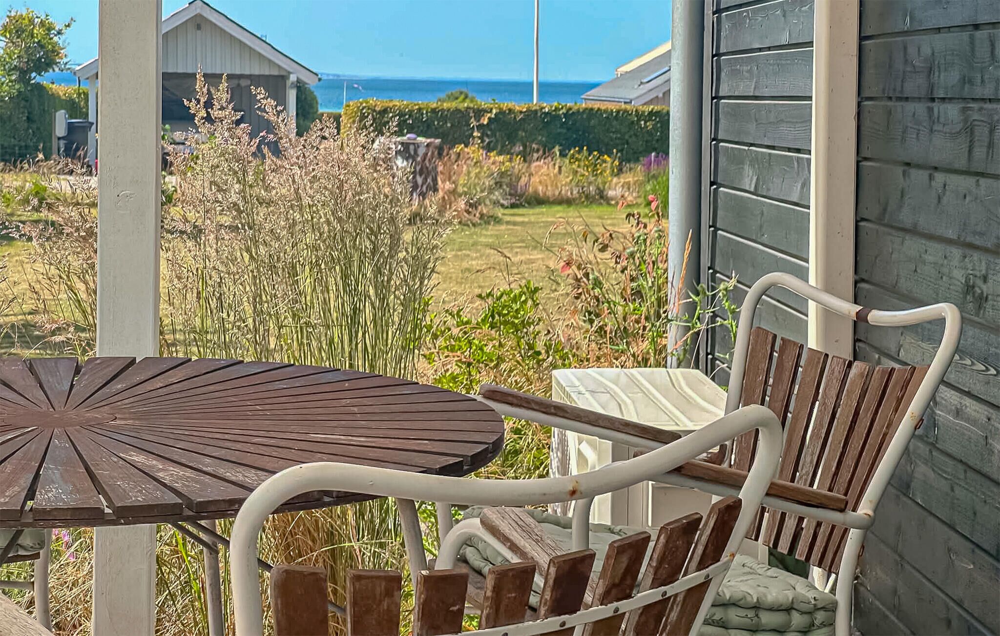 Een terras met een tafel en stoelen, met uitzicht op een tuin en de zee.