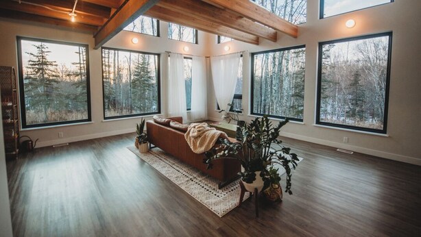Ein geräumiges Wohnzimmer mit großen Fenstern, einer Holzbalkendecke und einem gemütlichen Sofa.