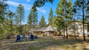A cabin with a covered porch, surrounded by trees, and a gravel ground. - Pine Grove Retreat for 10 | Game Room + Fire Pit (Pine Grove)
