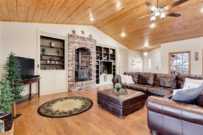 A living room with a brick fireplace, leather sofas, a television, and a ceiling fan.