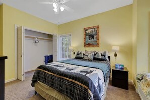 A bedroom with a bed, a wardrobe, a window, a ceiling fan, and a painting on the wall.