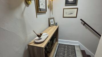 A hallway with a wooden console table, two wall-mounted lamps, framed artwork, a woven basket, and a patterned rug.