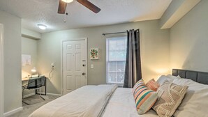 Un dormitorio con cama, escritorio, silla, ventilador de techo, ventana con cortinas y una lámpara de pared.