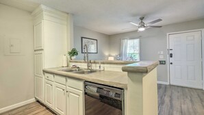 Una cocina con armarios blancos, lavavajillas, fregadero y ventilador de techo.