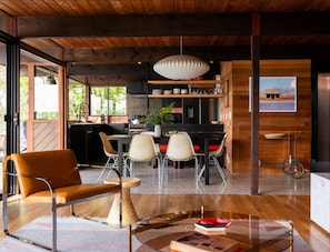 A modern kitchen with a dining area featuring a wooden table, chairs, and a coffee table. - Deck & Views: MCM Waterfront Port Orchard Retreat (Port Orchard)