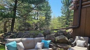 An outdoor patio with a sofa, armchair, and coffee table, surrounded by rocks and trees. - 5-bedroom cabin - Where peaceful vacationing meets nearby adventures  (Wisconsin Dells)