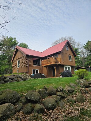 A two-story log cabin with a red roof, a balcony, and a stone wall in the foreground. - 5-bedroom cabin - Where peaceful vacationing meets nearby adventures  (Wisconsin Dells)