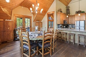 A rustic kitchen with wooden cabinets, a large island with stools, and a chandelier. - Deschutes Reserve- Riverfront Home with Hot Tub (Sunriver)