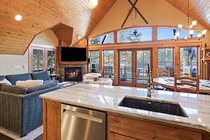 A spacious living area with a fireplace, a large TV, and a dining area with wooden furniture. - Deschutes Reserve- Riverfront Home with Hot Tub (Sunriver)