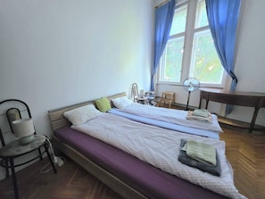 Ein Zimmer mit zwei Betten, einem Sessel, einem Schreibtisch und einem fenster mit Vorhängen.