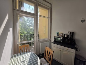 Eine kleine Küche mit Tisch und Stühlen, ein Fenster mit Blick auf Grünflächen und eine Arbeitsplatte mit Geräten.