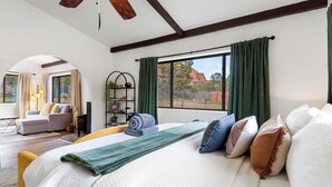 Ein Schlafzimmer mit Bett, Sofa, Leseecke und einem großen Fenster mit Vorhängen.