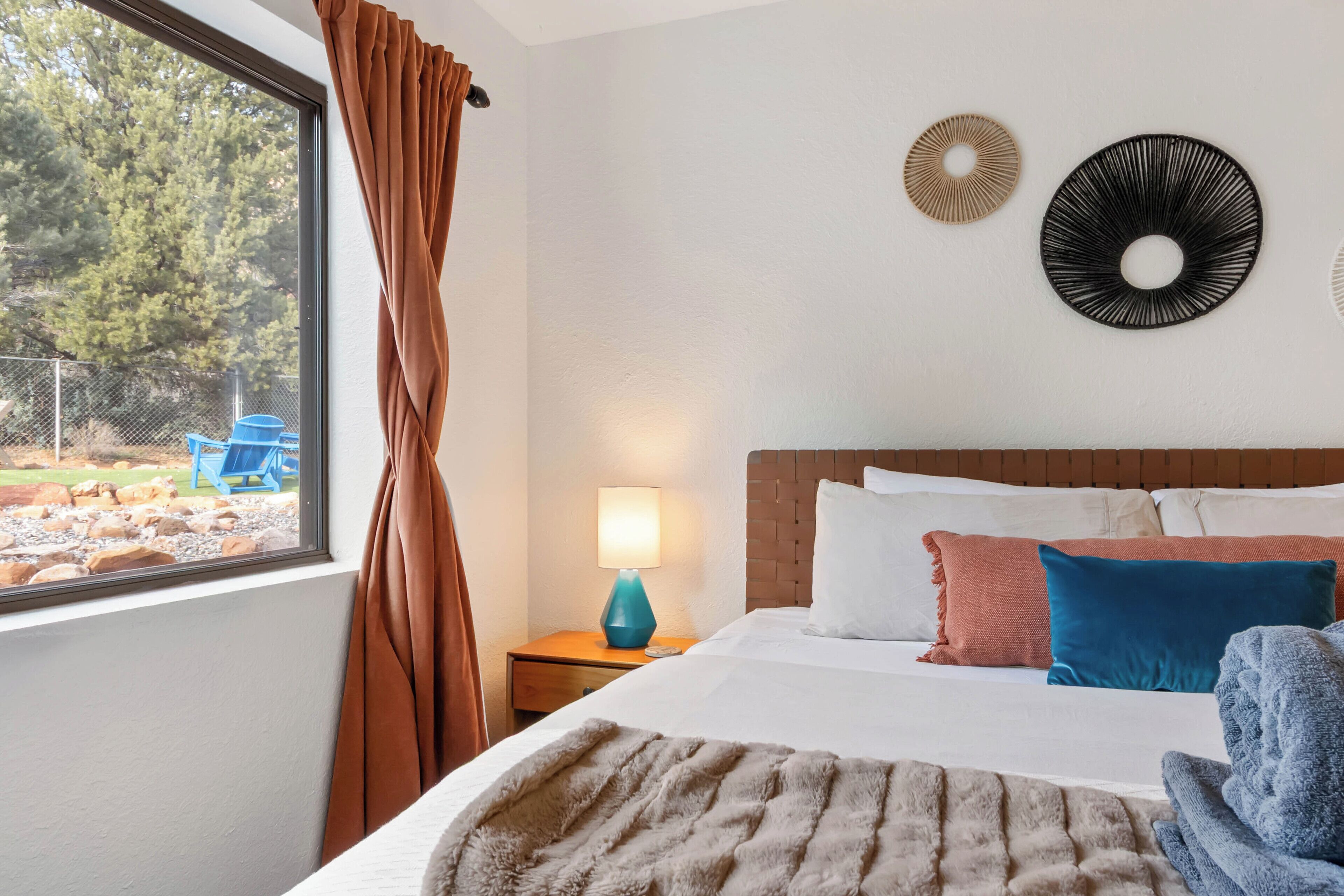 A hotel room with a large bed, a nightstand with a lamp, a view of the outdoors, and decorative wall art.