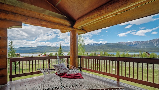 Une terrasse en bois avec un hamac, une couverture rouge et un coussin orné du mot « Sweet Cabin ».