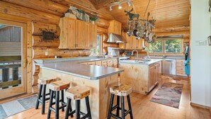 Une cuisine de style rustique, avec un îlot central, des tabourets de bar, des armoires en bois et un porte-ustensiles suspendu.