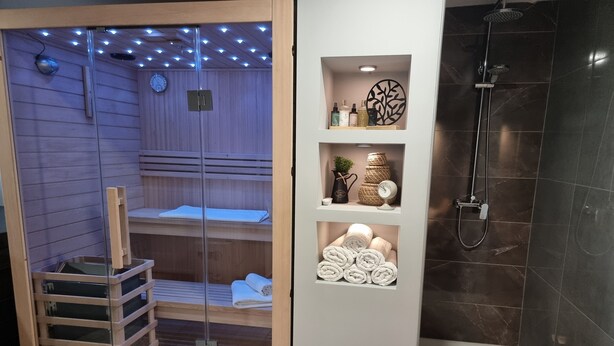 A sauna with a glass door, wooden benches, and a shelf with towels and toiletries. - Hilltop house with jacuzzi, sauna, pool, barbecue, and orchard (Voloder)