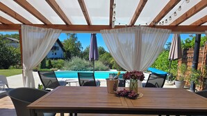 An outdoor patio with a wooden table, chairs, a pool, and a pergola with string lights. - Hilltop house with jacuzzi, sauna, pool, barbecue, and orchard (Voloder)