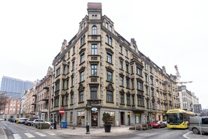 Ein historisches Gebäude mit mehreren Etagen, großen Fenstern und einem markanten Eingang in einer Hausecke.