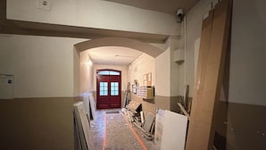 A hallway with a red door at the end, construction materials scattered on the floor, and a security camera on the wall. - Słowackiego Serene Studio with Balcony (Katowice)