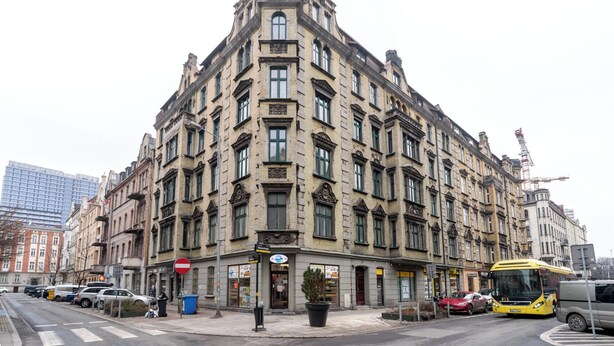 Ein historisches Gebäude mit mehreren Etagen, großen Fenstern und einem markanten Eingang in einer Hausecke.