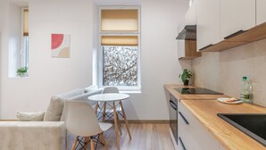 Eine kleine Küche mit Holzschränken, ein Essbereich mit weißem Tisch und Stühlen sowie ein Fenster mit Jalousien.