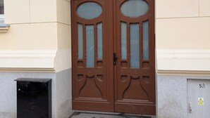Una puerta doble marrón con paneles de vidrio y molduras decorativas, un buzón negro pequeño y un timbre.