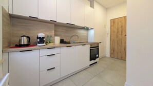 Una cocina moderna con armarios blancos, un hervidor de acero inoxidable, una cafetera y una puerta de madera.