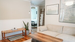 A living room with a wooden bench, a white sofa, a potted plant, and a framed picture on the wall. - Soothing 2-bedroom cottage with Sauna in Old Orchard Beach (Old Orchard Beach)