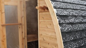 A wooden sauna with a glass door, attached to a building with a sloped roof covered in snow. - Soothing 2-bedroom cottage with Sauna in Old Orchard Beach (Old Orchard Beach)