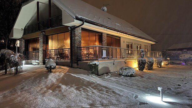 Une maison à deux étages, dont le toit est recouvert de neige et dont le porche avant est illuminé.
