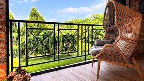 Un balcon avec un fauteuil en osier, une vue sur la verdure et un mur en briques.