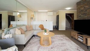 Ein modernes Wohnzimmer mit einer Couch, einem runden Couchtisch, einem Flachbildfernseher und einer Treppe zu einer oberen Ebene.