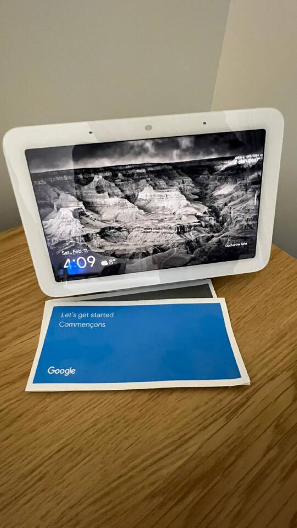 A tablet on a wooden table displaying a black and white landscape image with a date and time.