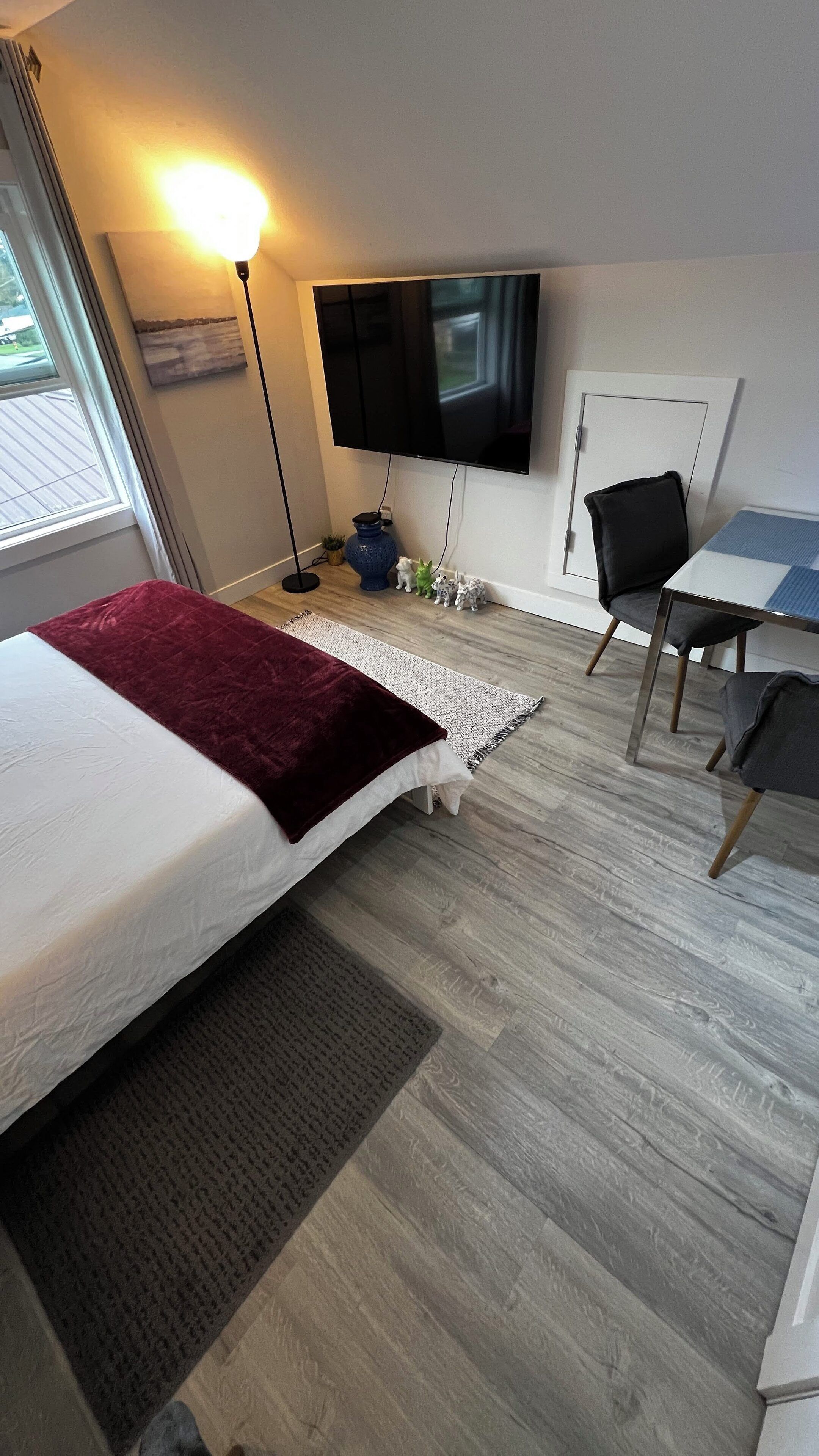 A bedroom with a bed, a desk, a chair, a TV, and a window.