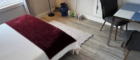 A bedroom with a bed, a desk, a chair, a TV, and a window.