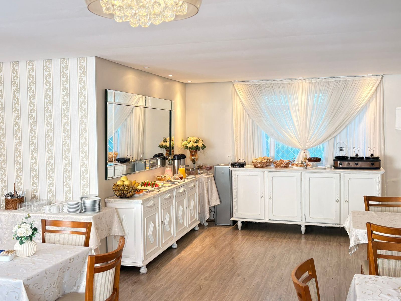 A dining area with a buffet setup, a large mirror, and a chandelier.