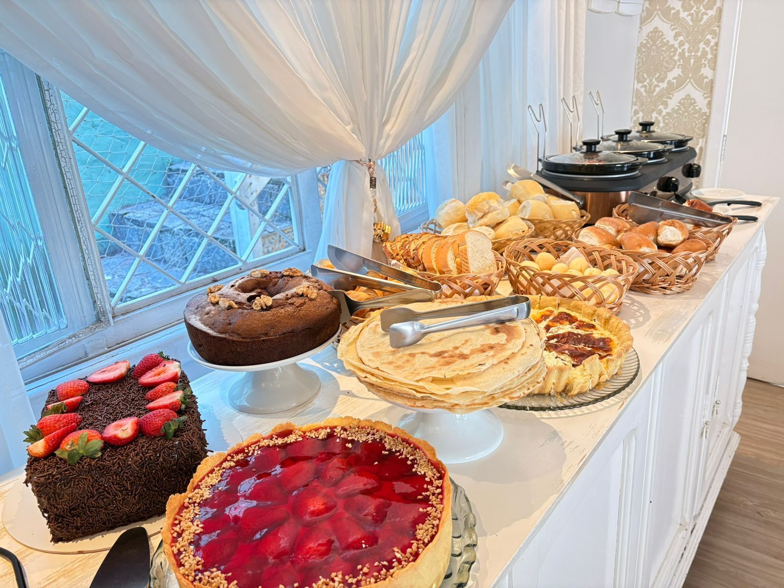 A buffet with various desserts including a chocolate cake, a strawberry tart, and multiple types of bread and pastries.