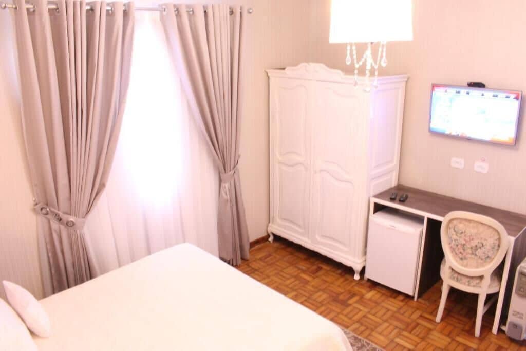 A bedroom with a bed, a desk, a chair, a wardrobe, and a television on the wall.