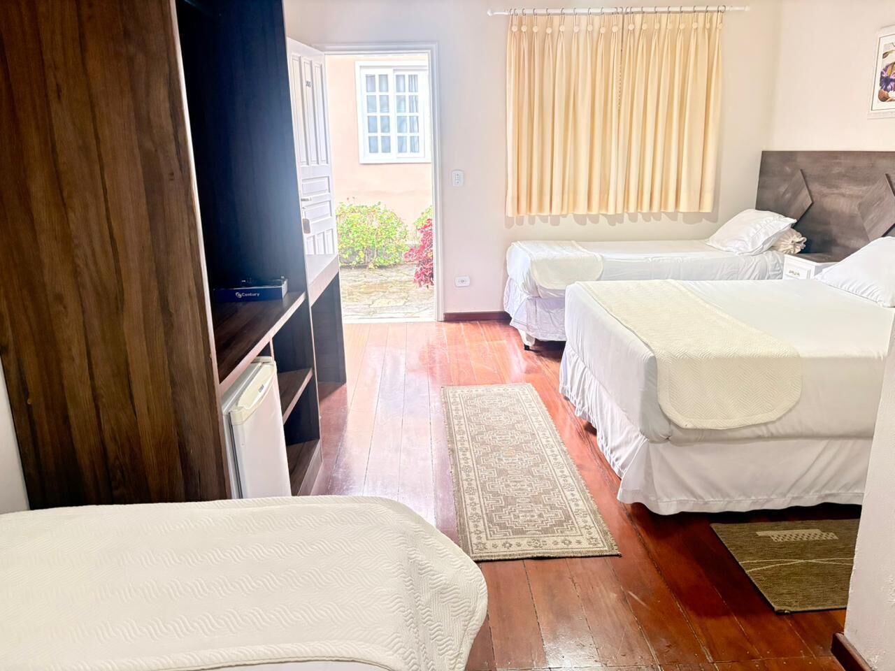 Quarto com duas camas, guarda-roupa de madeira, televisão e vista para o exterior.