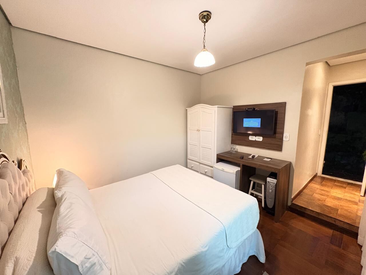 A bedroom with a bed, a desk, a television, and a wardrobe.