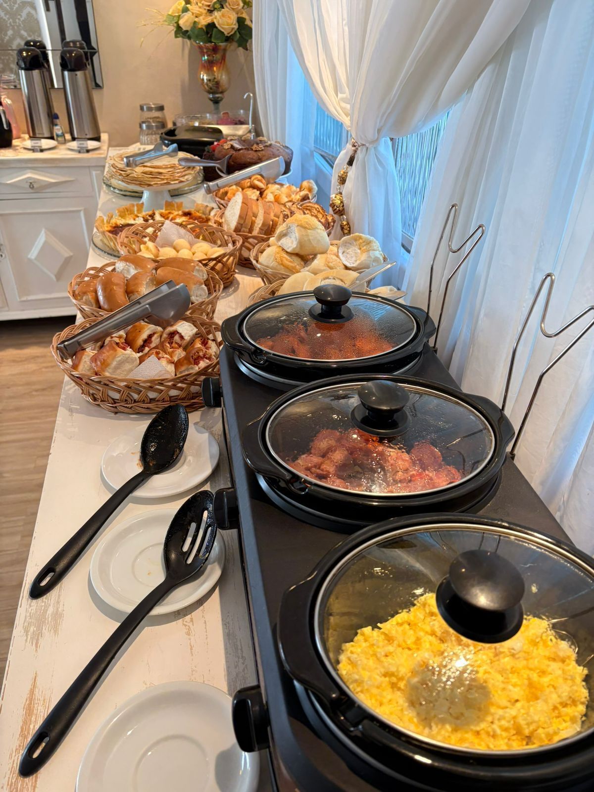 A buffet setup with various food items, including bread, pastries, and covered dishes.