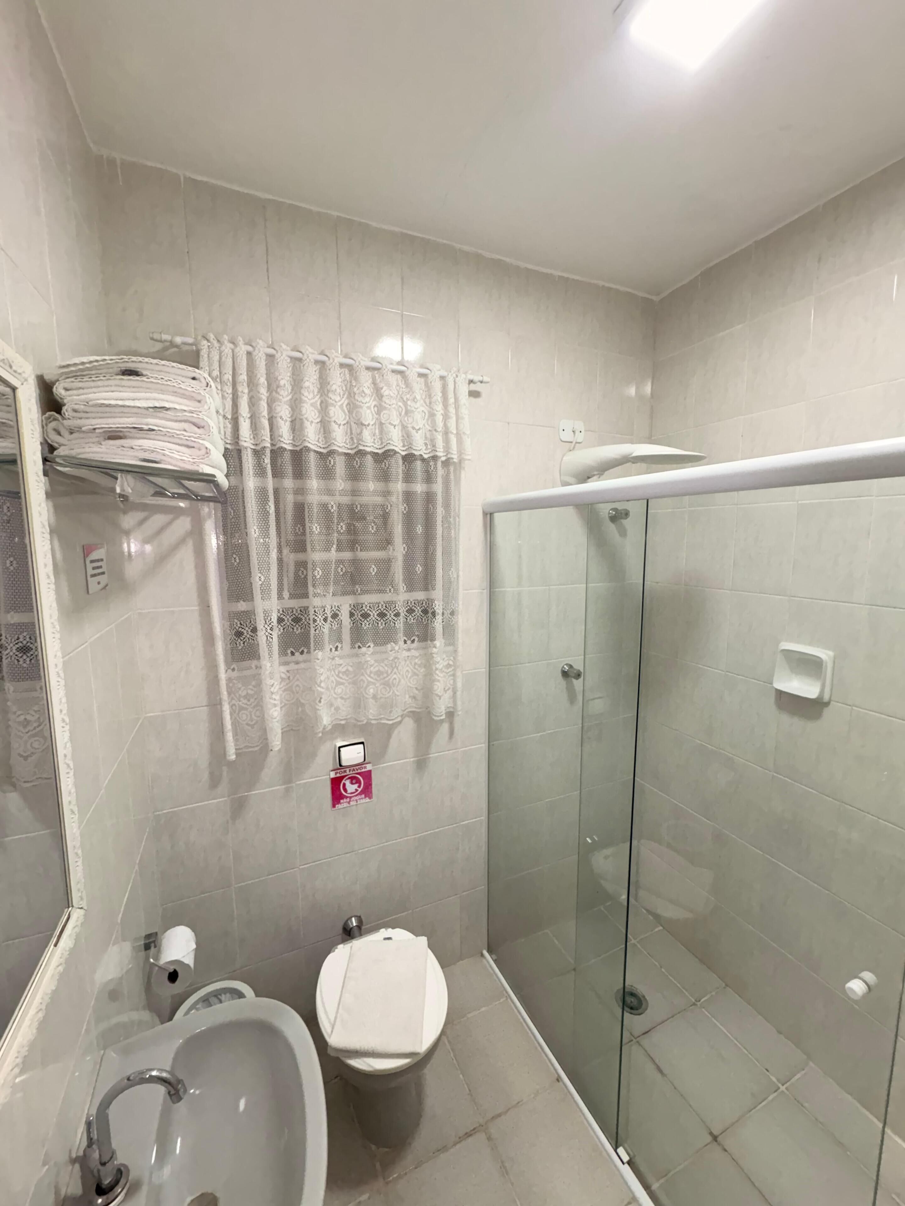 A bathroom with a glass shower enclosure, a toilet, a sink, and a towel rack with folded towels.